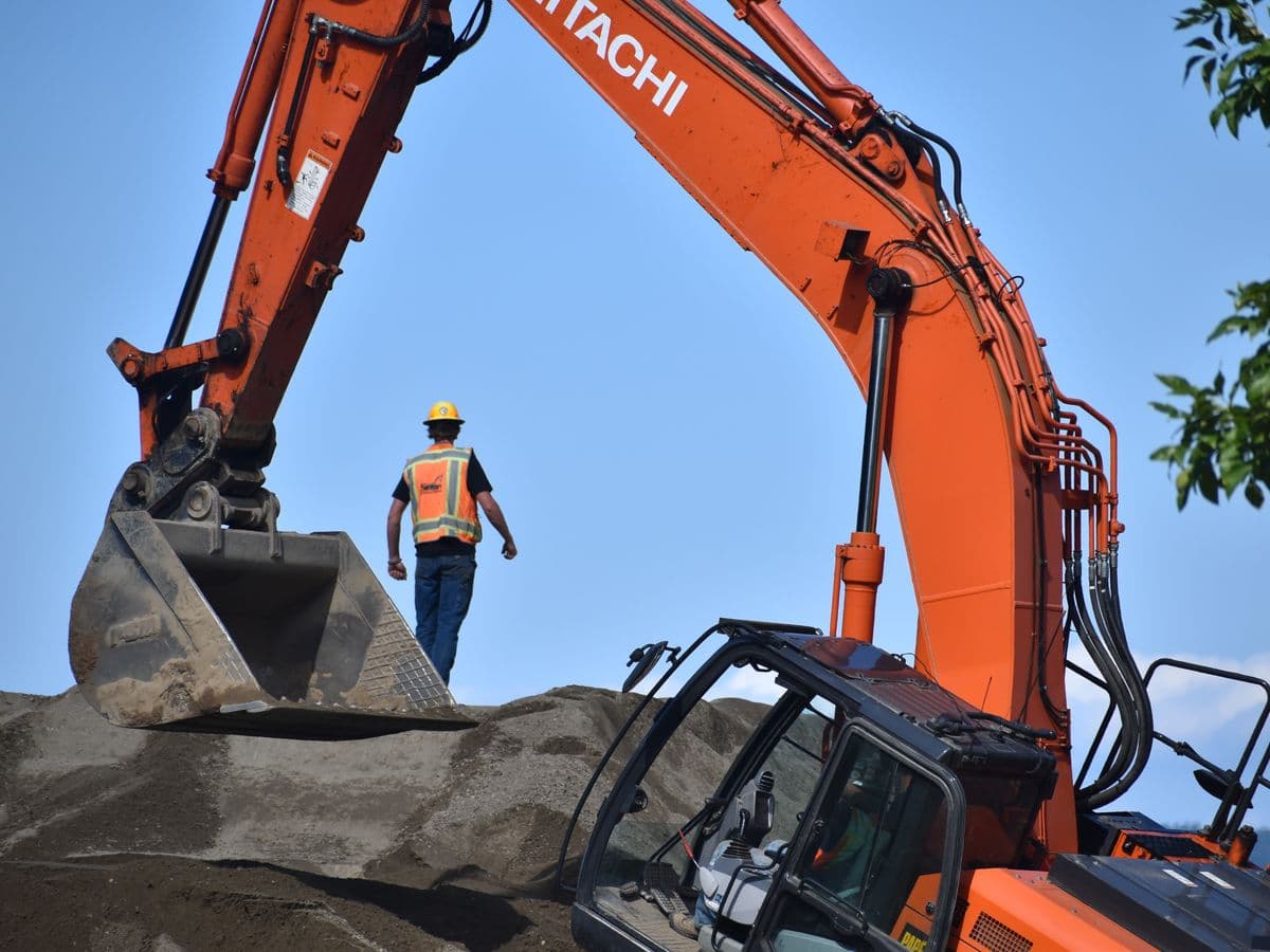 Contractor inspecting the hydraulic lines and undercarriage of a used excavator